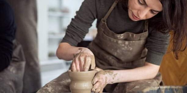 Young woman artist making clay bowl on pottery wheel